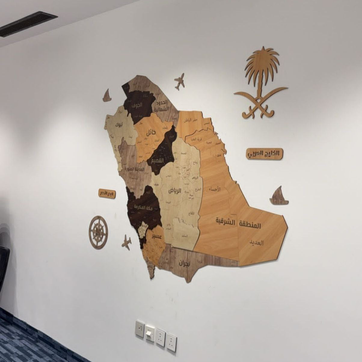 Wooden map of Saudi Arabia on a white wall with decorative elements.